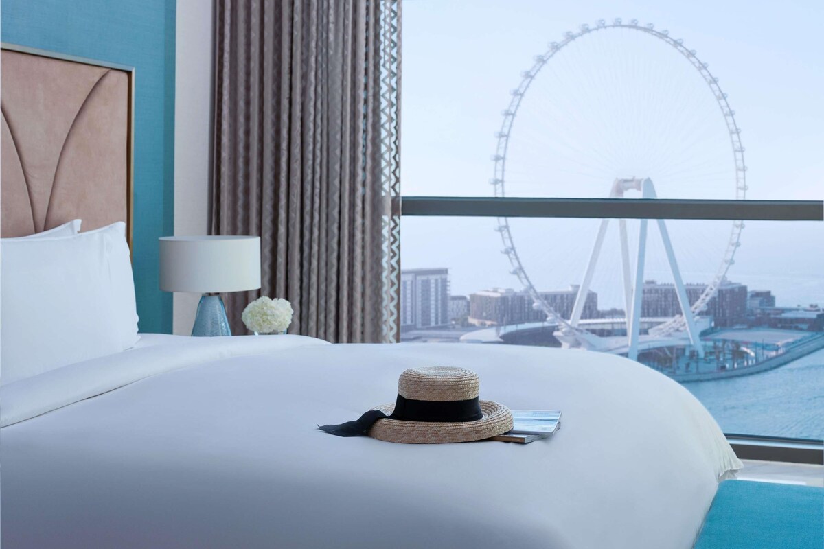 Une chambre d’hôtel avec un lit, une lampe, un chapeau et une vue sur une grande roue.