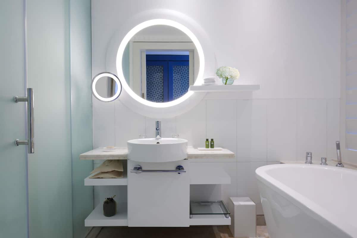 Un baño moderno con un espejo redondo, un lavabo, una bañera y un estante con artículos de aseo.