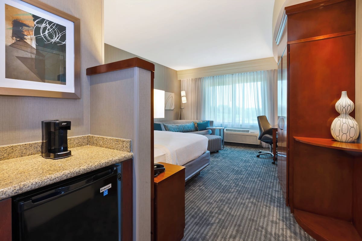 Habitación de hotel con kitchenette, una cama, escritorio y un ventanal con cortinas.