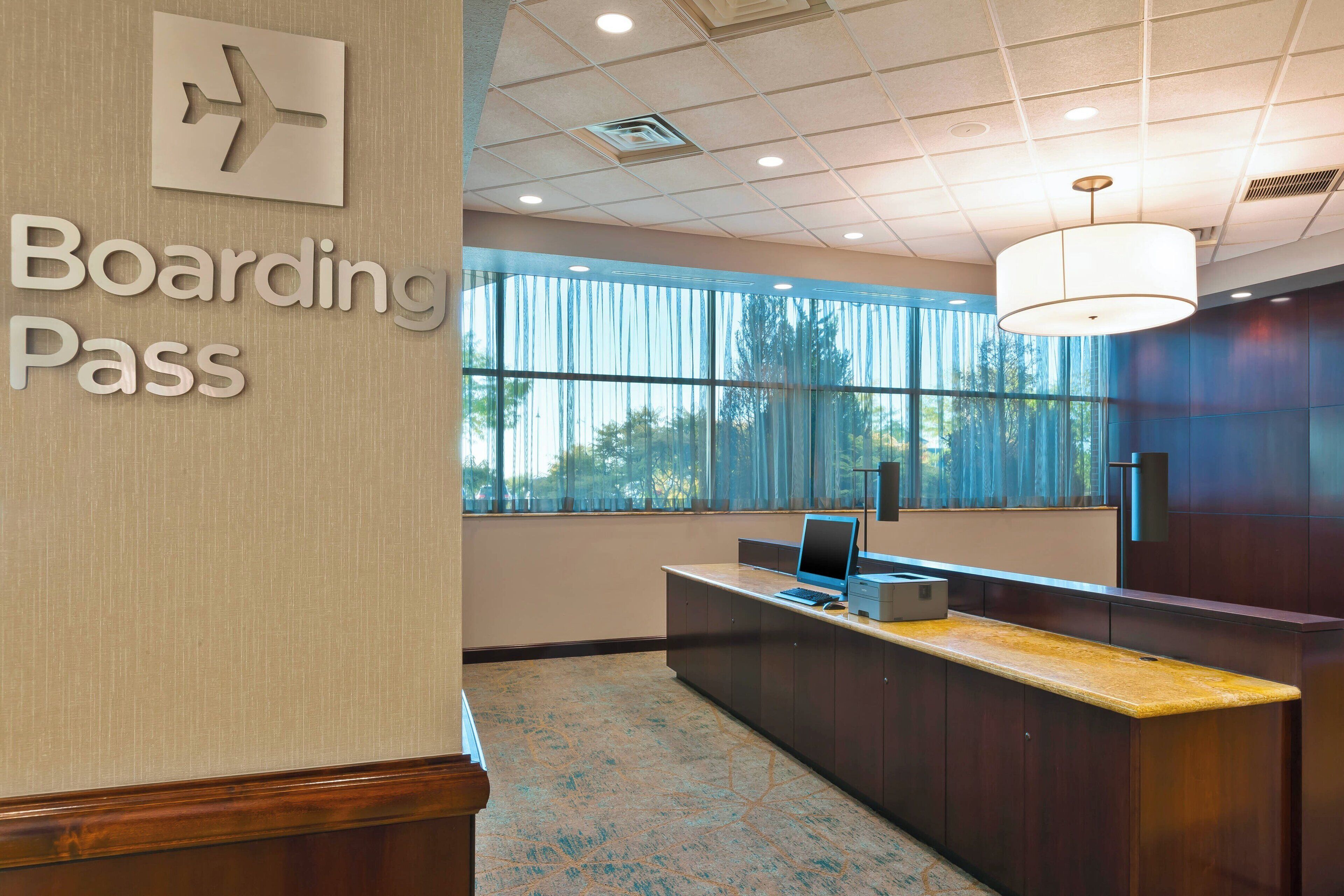 A modern reception area with a 'Boarding Pass' sign, a desk, and large windows.