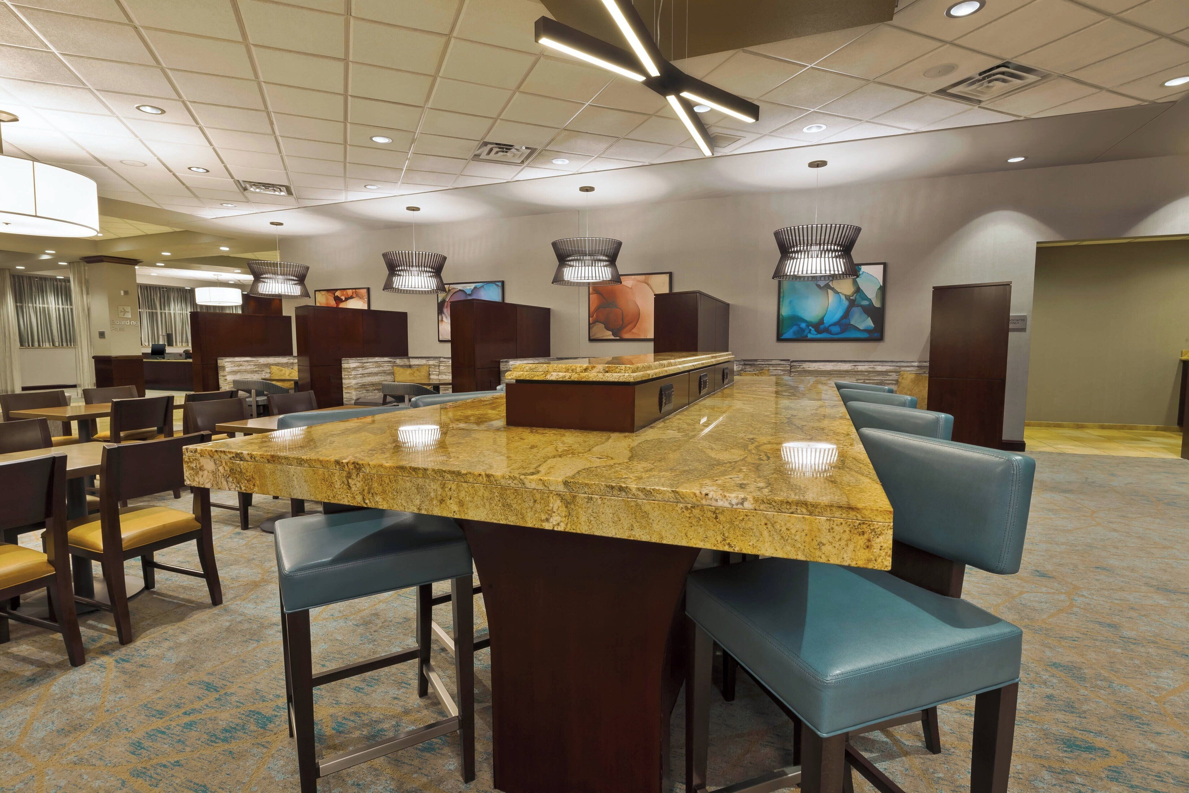 A modern hotel lobby with a long marble bar, comfortable seating, and contemporary lighting fixtures.