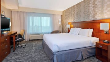 Une chambre d’hôtel avec un grand lit, un bureau avec une chaise, une télévision et une fenêtre avec des rideaux.
