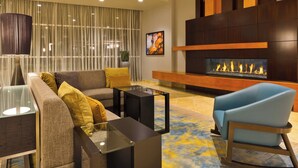 A modern living room with a sofa, armchairs, a glass coffee table, and a fireplace. - Courtyard by Marriott Omaha La Vista (La Vista)