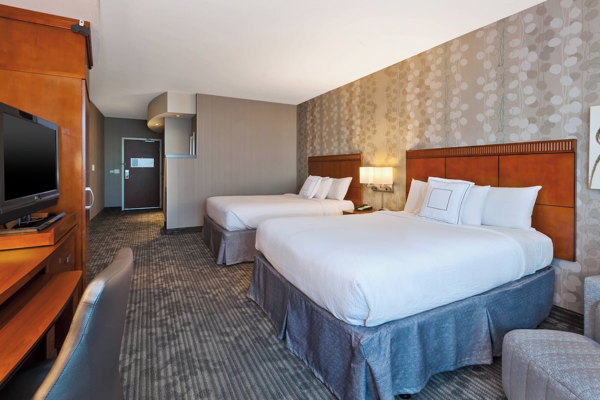 Habitación de hotel con dos camas, televisión, escritorio y baño.