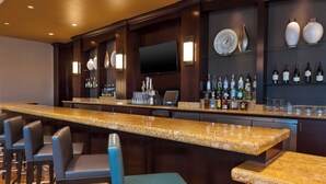 A bar area with a long counter, multiple bar stools, and a television mounted on the wall. - Courtyard by Marriott Omaha La Vista (La Vista)