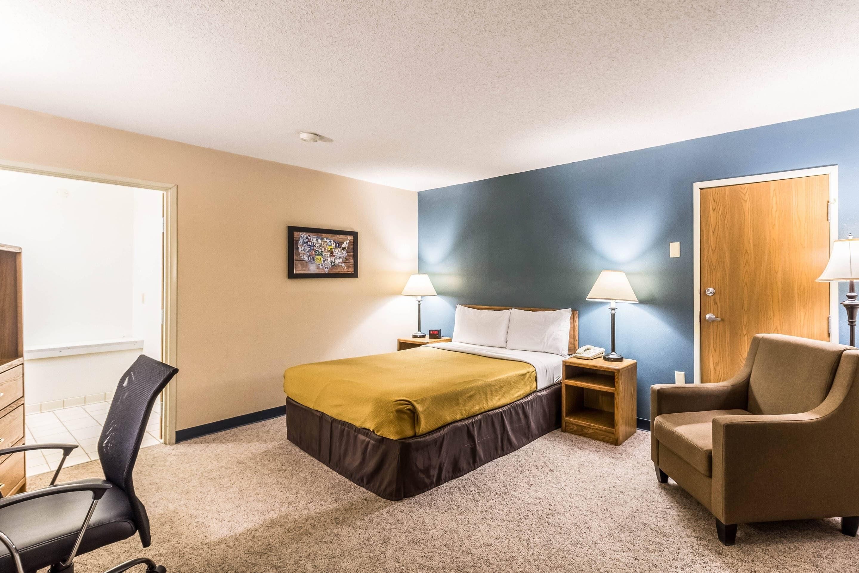 A hotel room with a bed, two bedside tables, a chair, a desk, and a door.