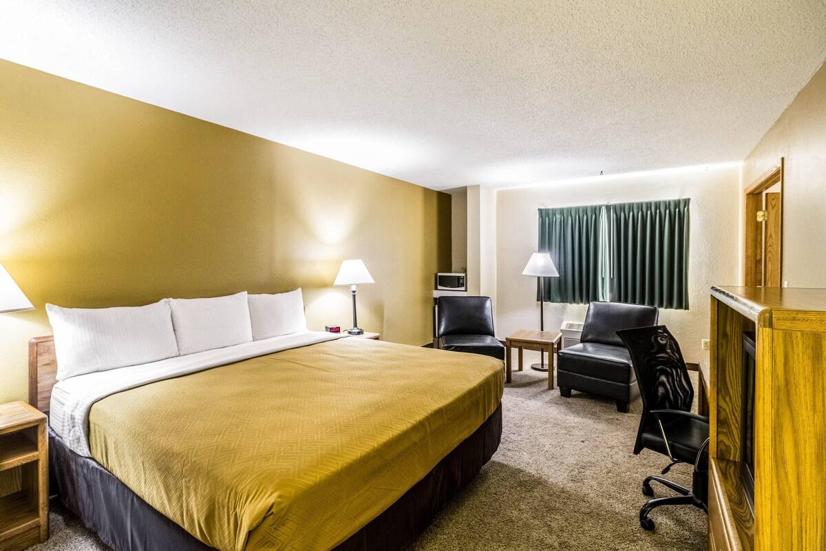 A hotel room with a large bed, two chairs, a desk, and a television.