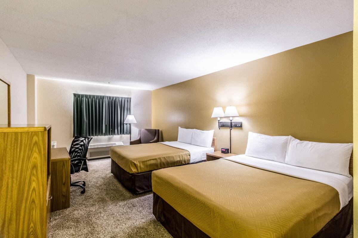 A hotel room with two beds, a desk, a chair, and a window with curtains.