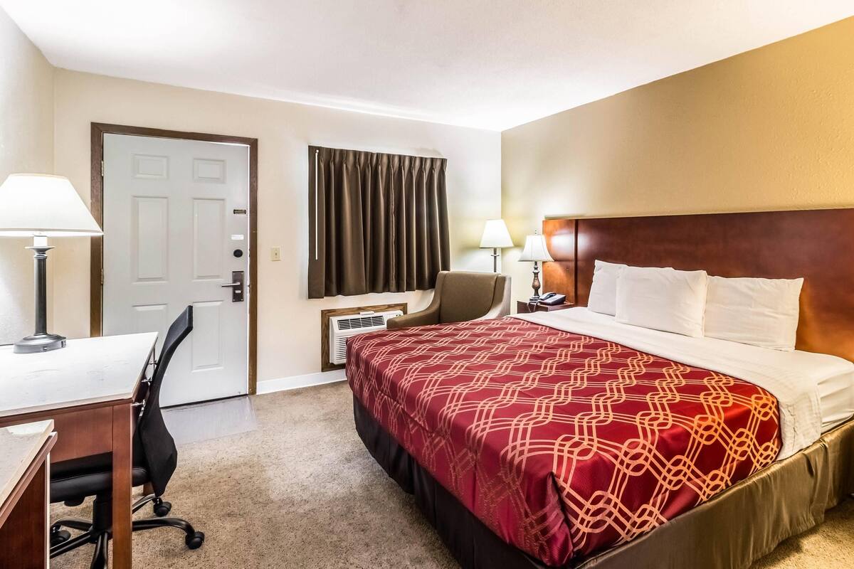 A hotel room with a bed, desk, chair, and a door.