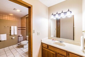 A bathroom with a white sink, wooden vanity, and a large mirror with lights. There is a toilet and a towel rack visible. - Econo Lodge Valley City (Valley City)