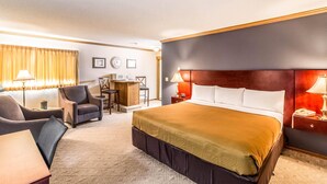 A hotel room with a large bed, a desk, a chair, a lamp, and a clock on the wall.