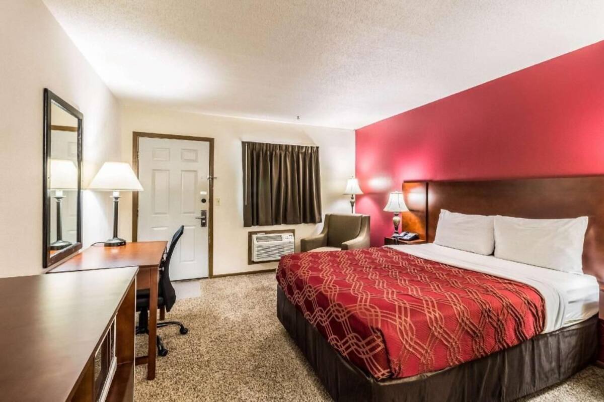 A hotel room with a bed, desk, chair, and a door.