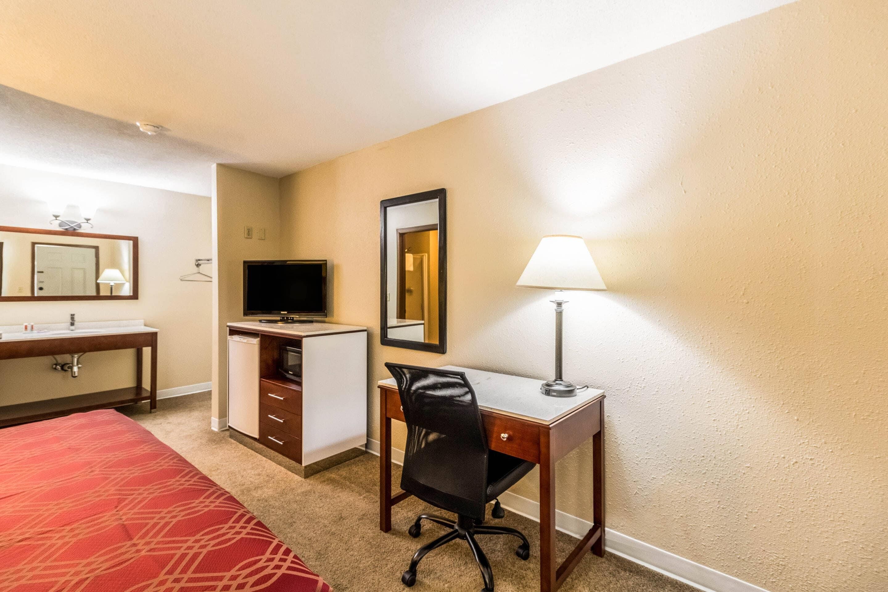 A hotel room with a bed, a desk, a chair, a television, a lamp, a mirror, and a wardrobe.