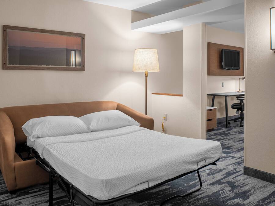 Habitación de hotel con cama, escritorio, silla, lámpara y televisor montado en la pared.
