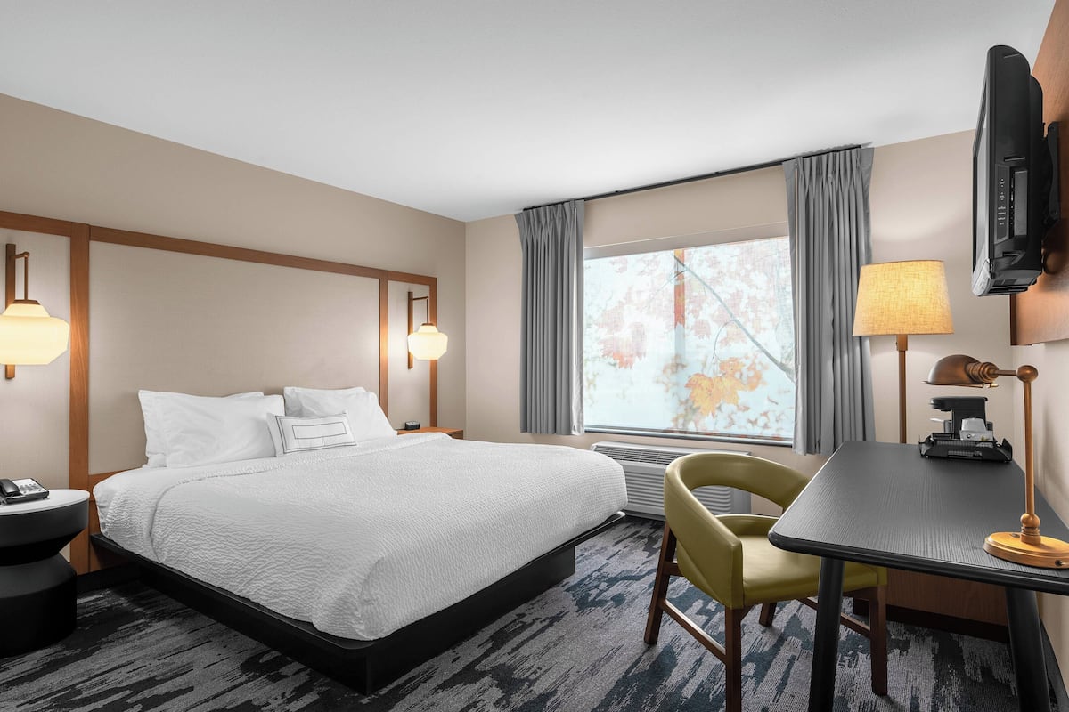 A hotel room with a large bed, a desk with a lamp, a chair, and a television mounted on the wall.