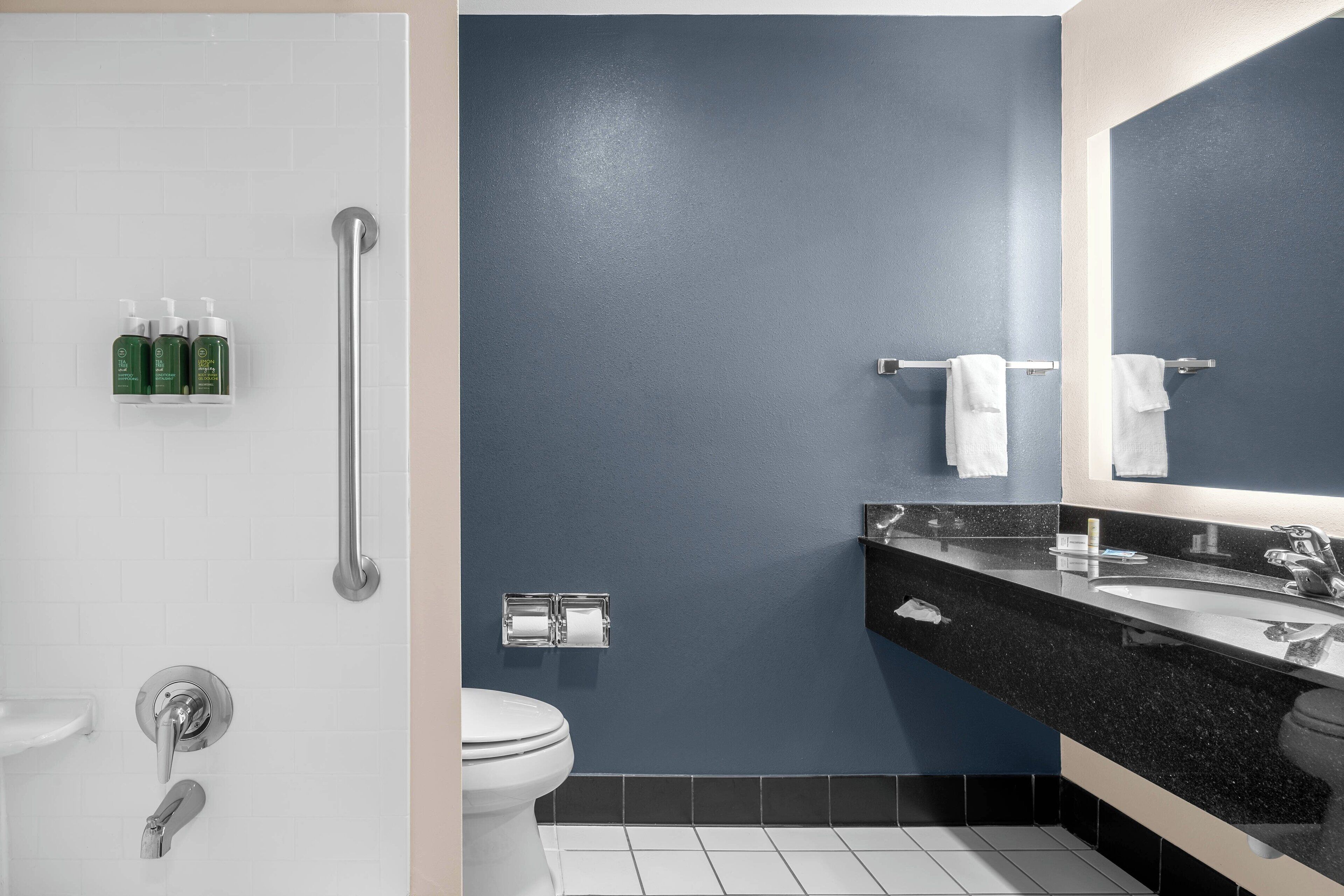 Un baño moderno con inodoro blanco, lavamanos con encimera negra, espejo y barandilla.