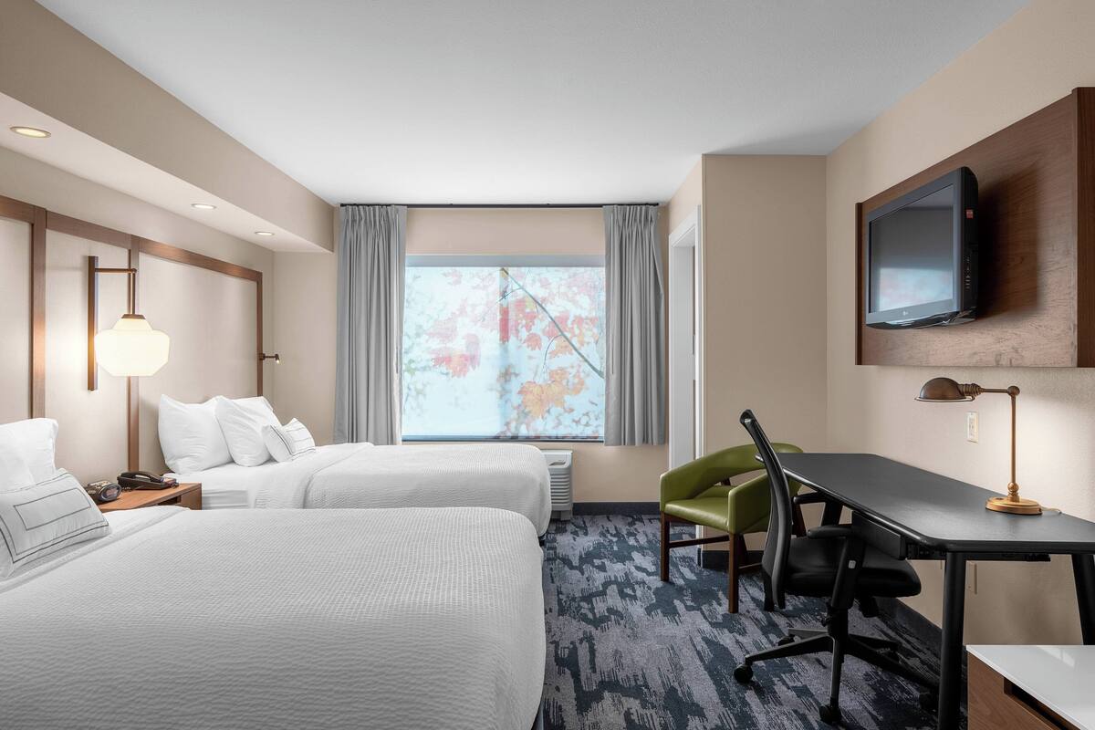 A hotel room with two beds, a desk, a chair, a TV, and a window with curtains.