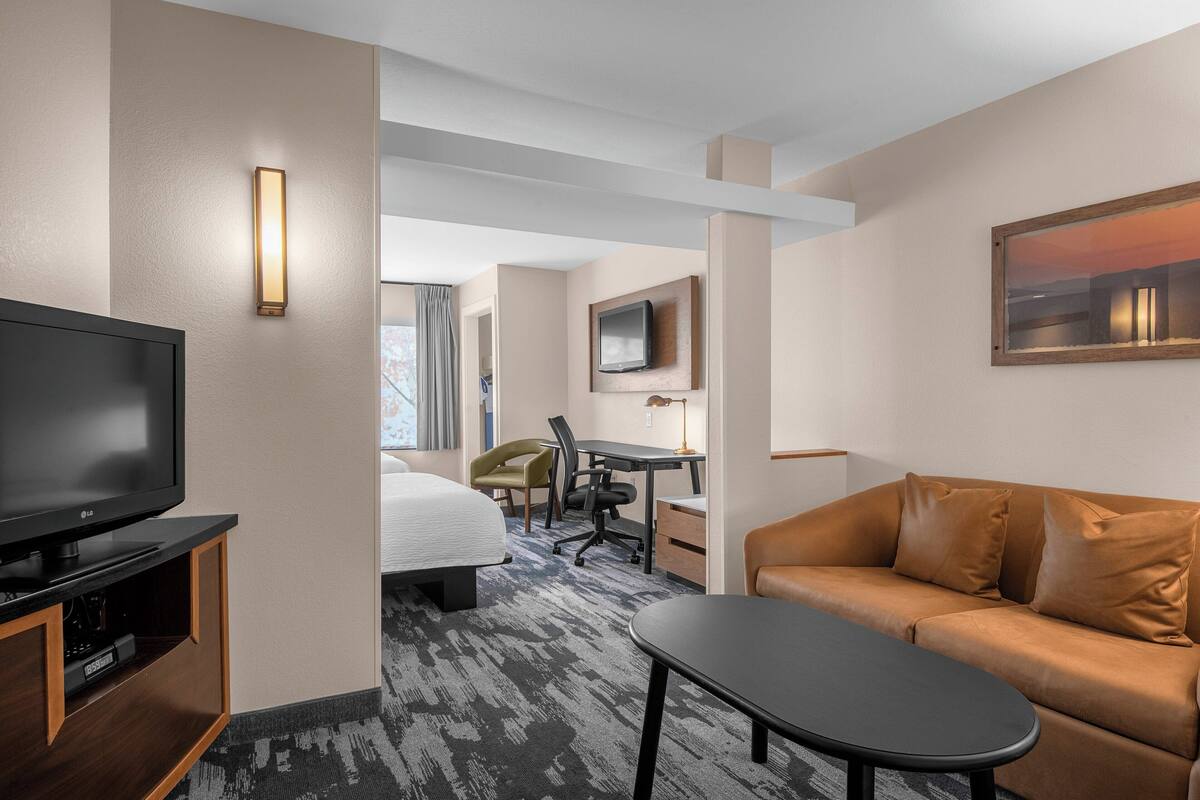 A hotel room with a bed, a TV, a desk, a chair, a sofa, and a painting on the wall.