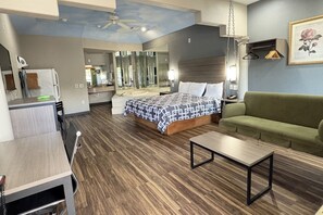 A hotel room with a bed, a green sofa, a wooden table, a desk, a mirror, and a ceiling fan.