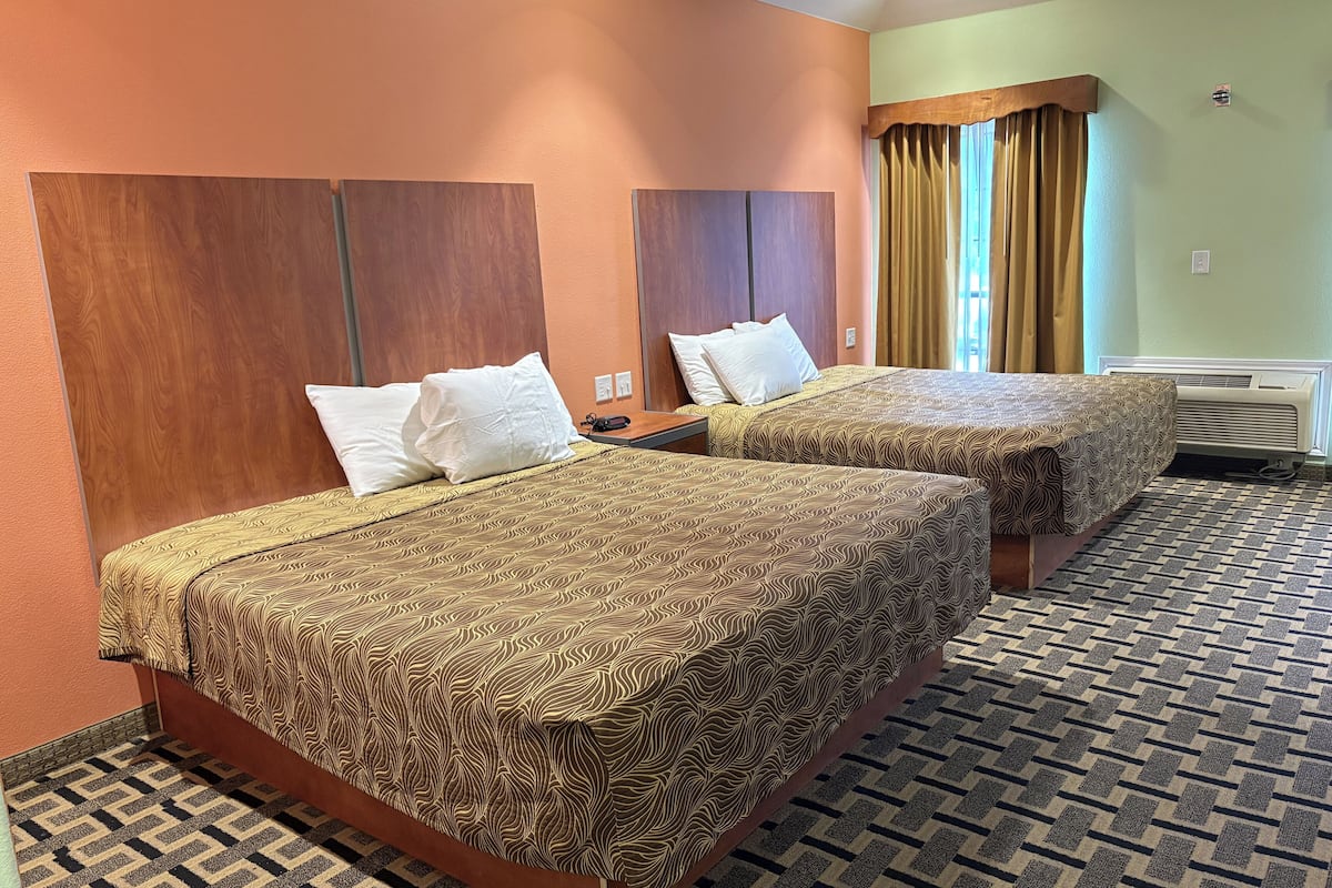 Habitación de hotel con dos camas, cada una con ropa de cama estampada y cabeceros de madera.