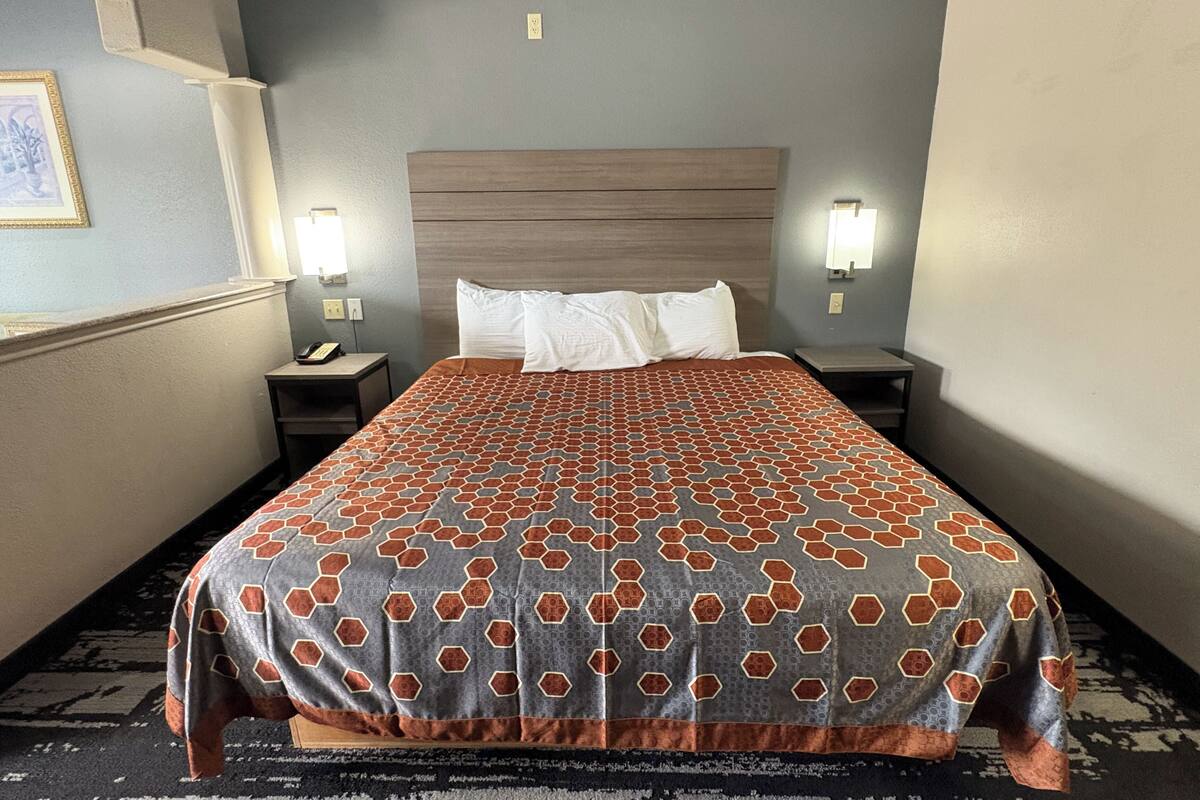 Habitación de hotel con una cama grande, dos mesitas de noche, una lámpara de pared e imagen en el marco.