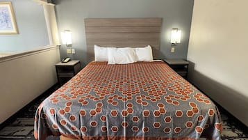 A hotel room with a large bed, two bedside tables, a nightstand, a wall-mounted lamp, and a framed picture on the wall.