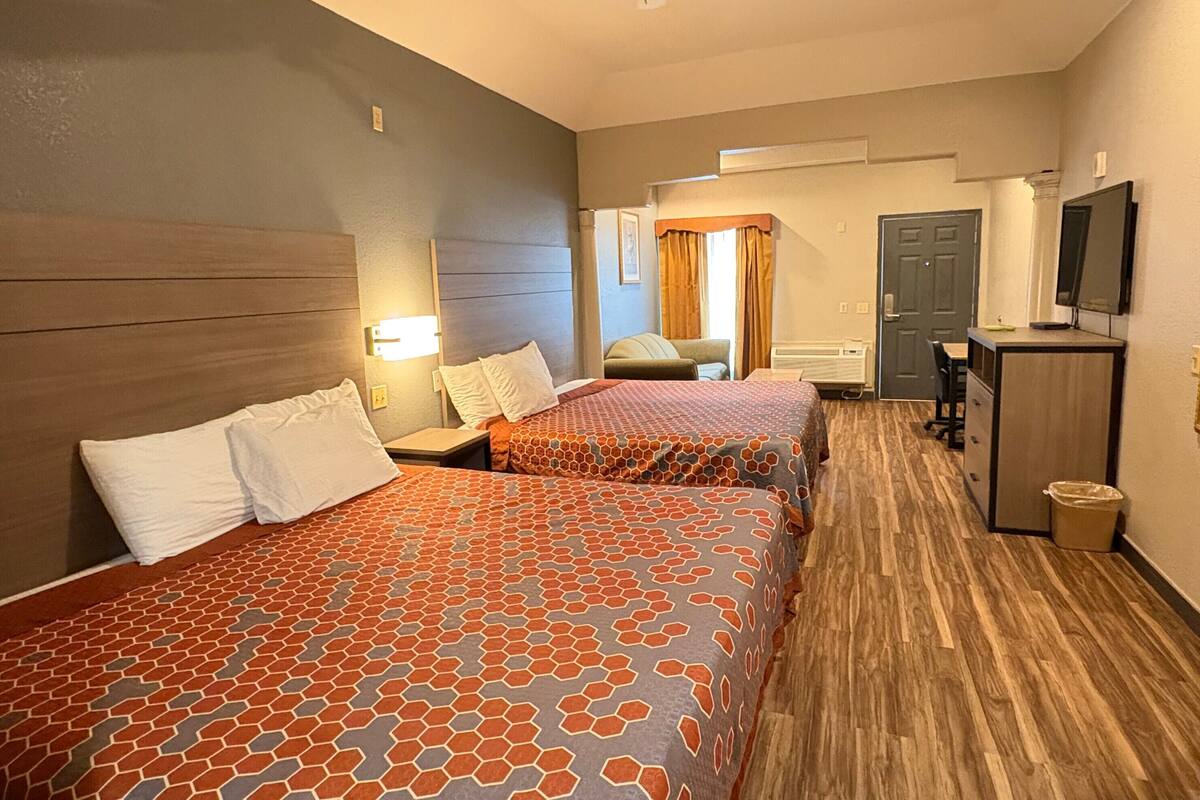 Habitación de hotel con dos camas, un escritorio, una silla, un televisor y un cesto de basura.