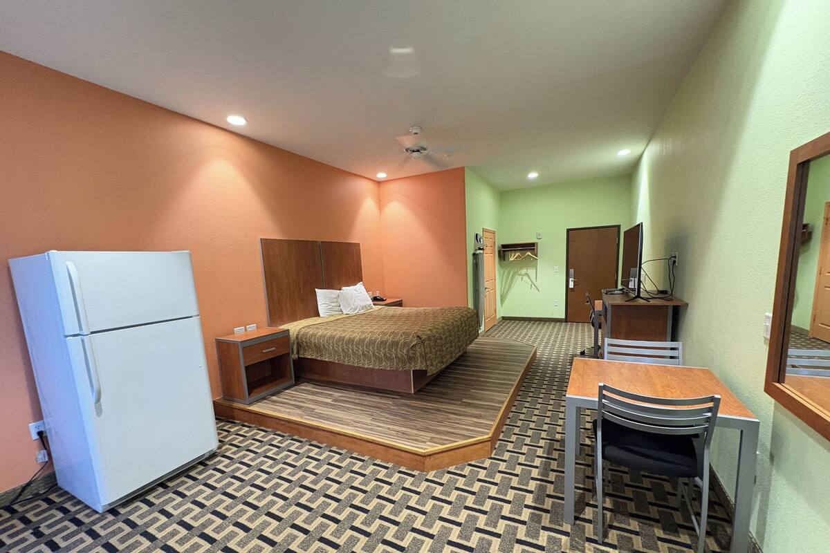 Una habitación de hotel con cama, escritorio, silla, refrigerador y espejo.