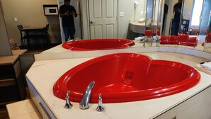 Ein modernes Badezimmer mit einer großen, roten Badewanne, einem weißen Waschbecken und einem Spiegel darüber.