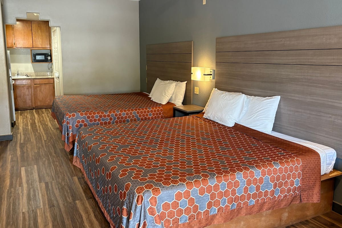 Una habitación de hotel con dos camas, una kitchenette y una mesita de noche con lámpara.