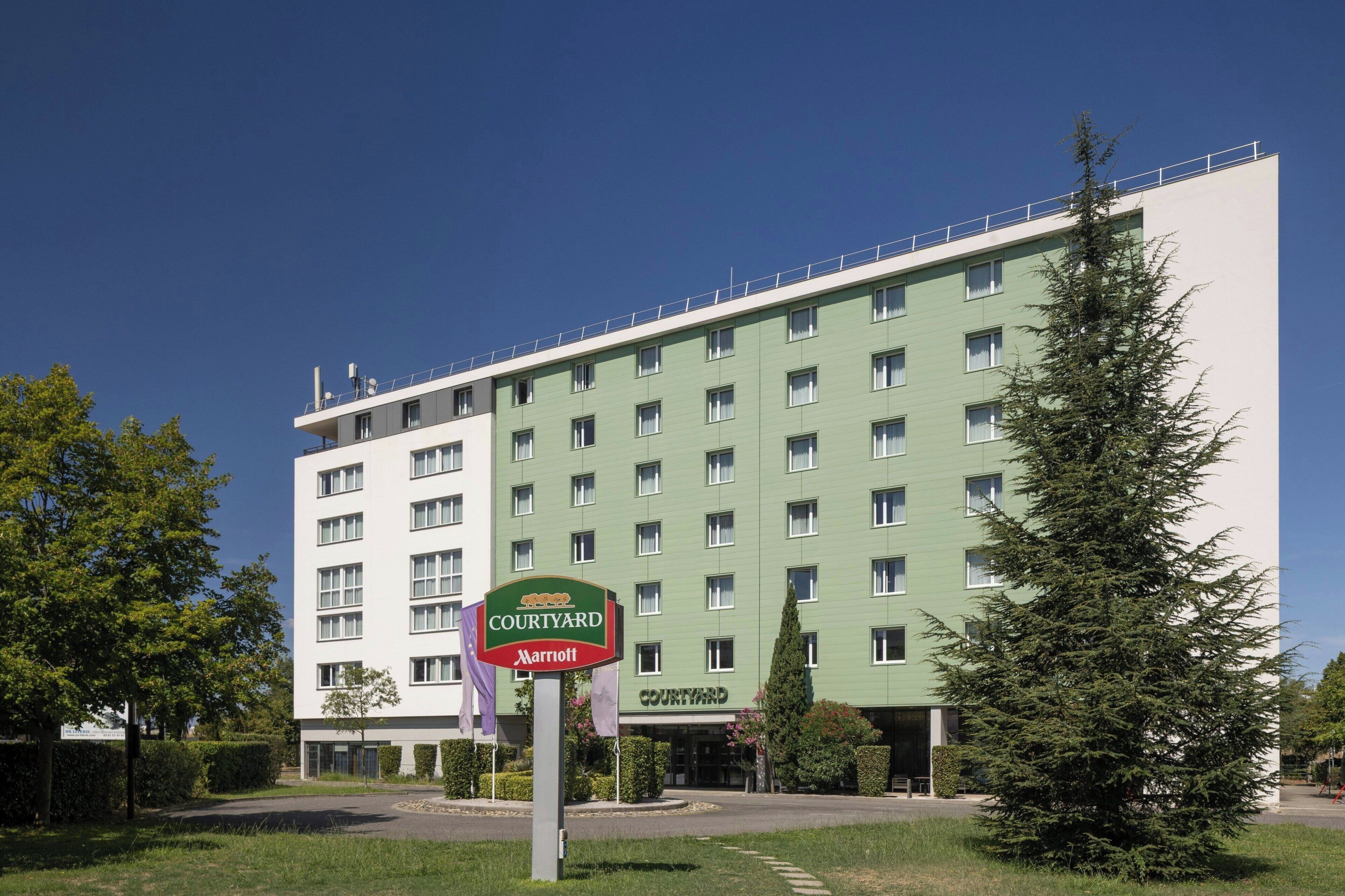 Un hôtel Courtyard Marriott à la façade verdoyante, doté de nombreuses fenêtres et d’une enseigne à l’avant.