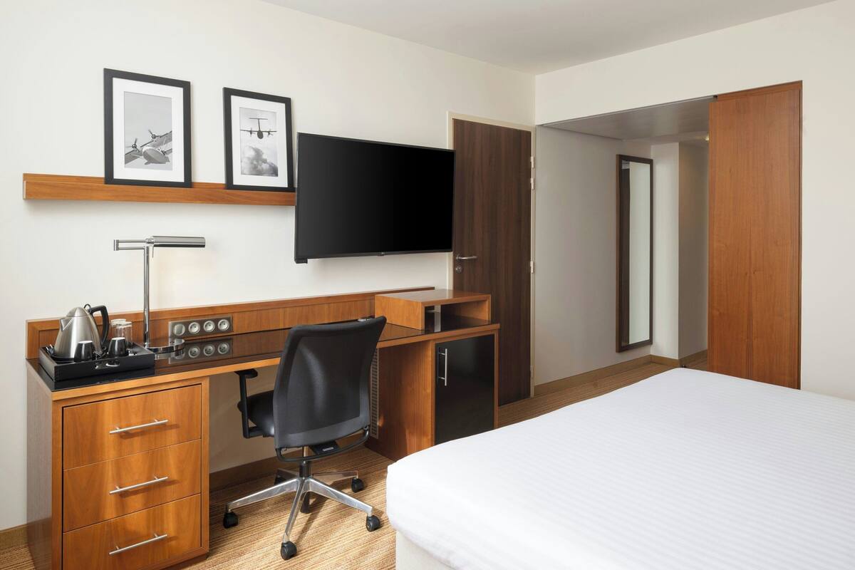 Une chambre d’hôtel avec un bureau en bois, un fauteuil de bureau noir, un téléviseur à écran plat, un lit et une armoire.