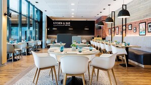 A modern restaurant with round tables, white chairs, and a brick wall.