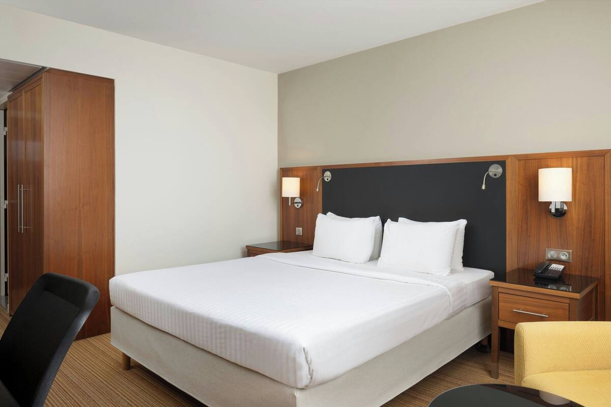 Une chambre d’hôtel avec un grand lit, deux tables de chevet avec des lampes, une armoire en bois, une chaise et une petite table.