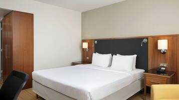 Ein Hotelzimmer mit einem großen Bett, zwei Nachttischen mit Lampen, einem Holzschrank, einem Stuhl und einem kleinen Tisch.