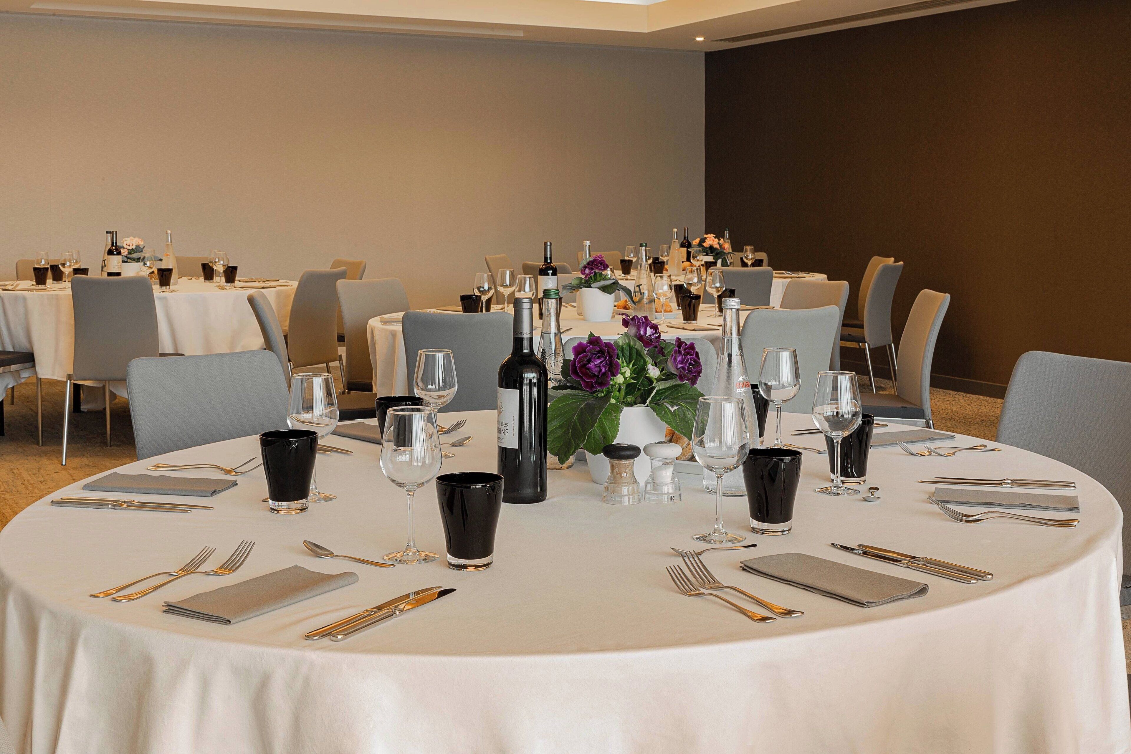 A dining area with round tables set for a meal, each with cutlery, glasses, and bottles.