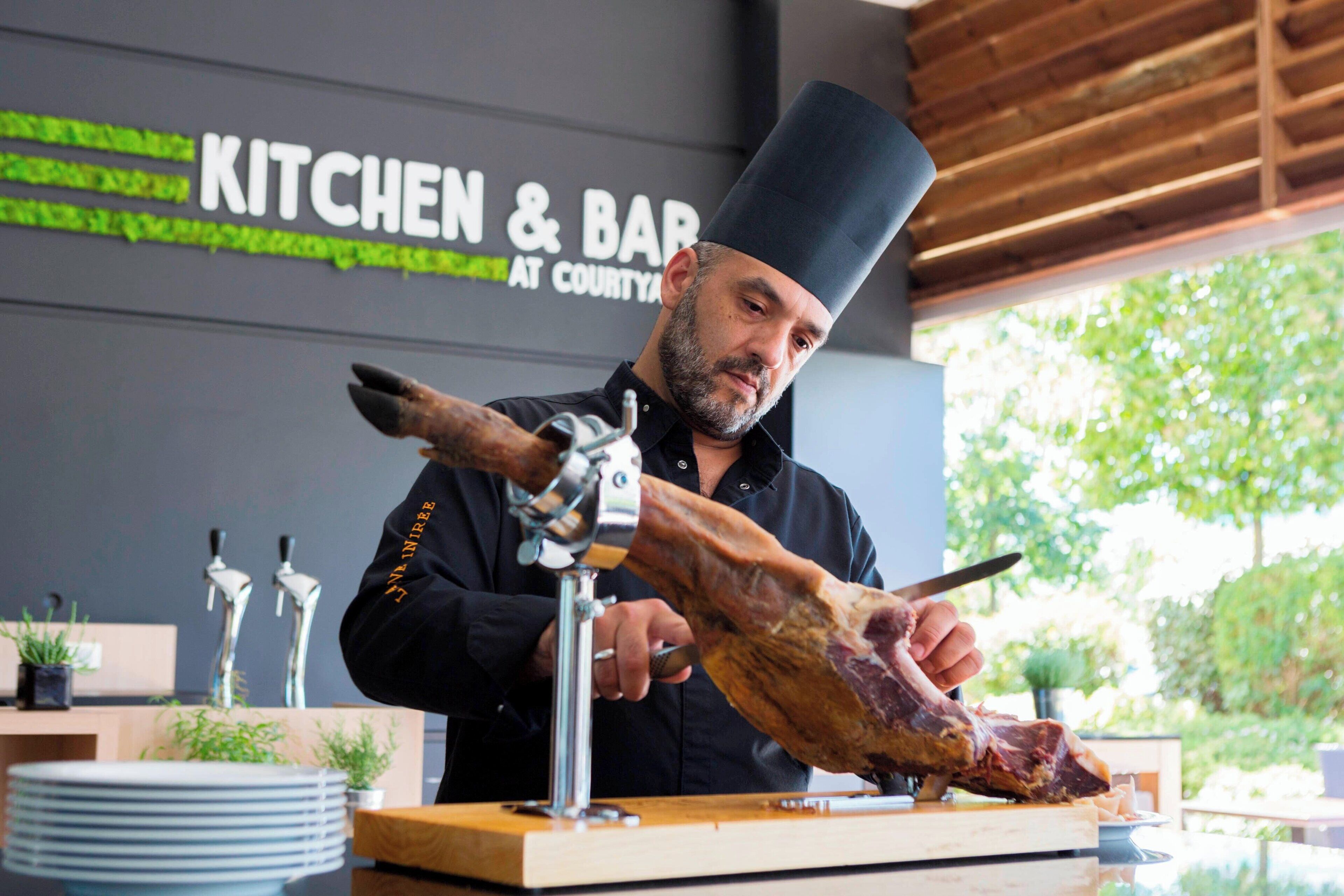 Un chef corta un gran trozo de carne sobre una tabla de madera en una cocina.