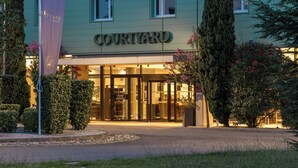 A Courtyard by Marriott hotel entrance with a glass facade, a sign above the entrance, and a well-maintained garden area.