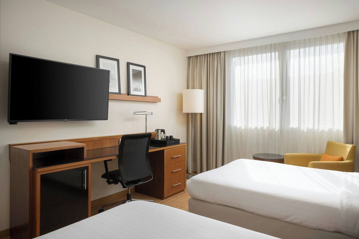Une chambre d’hôtel équipée d’un lit, d’un bureau, d’une chaise, d’une télévision, d’une lampe et d’une fenêtre avec des rideaux.