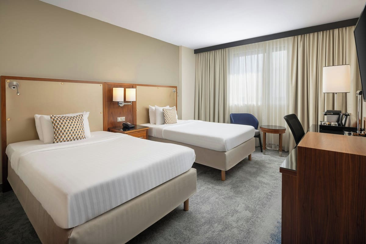 Une chambre d’hôtel avec deux lits, un bureau, une chaise, une petite table et un téléviseur.