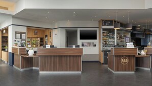 A modern hotel lobby with reception desks, a bar area, and a seating section.