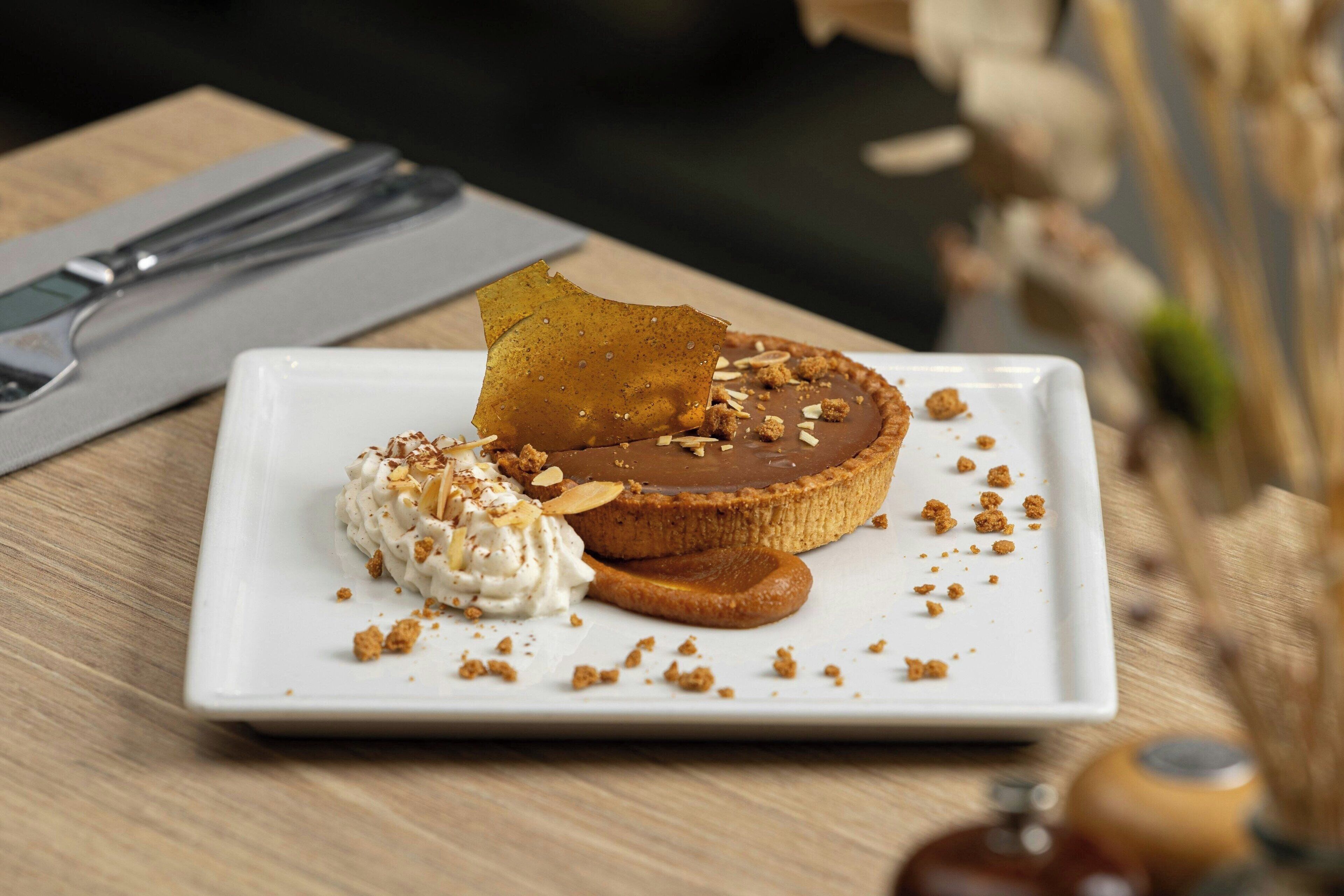 Un postre sobre un plato blanco, con una servilleta y cubiertos al fondo.