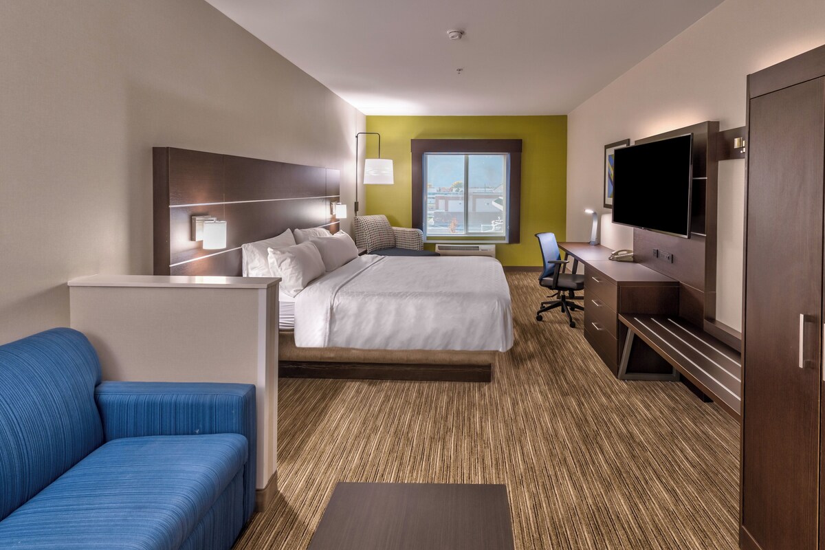 Une chambre d’hôtel avec un lit, un bureau, une télévision, un canapé bleu et une grande fenêtre.