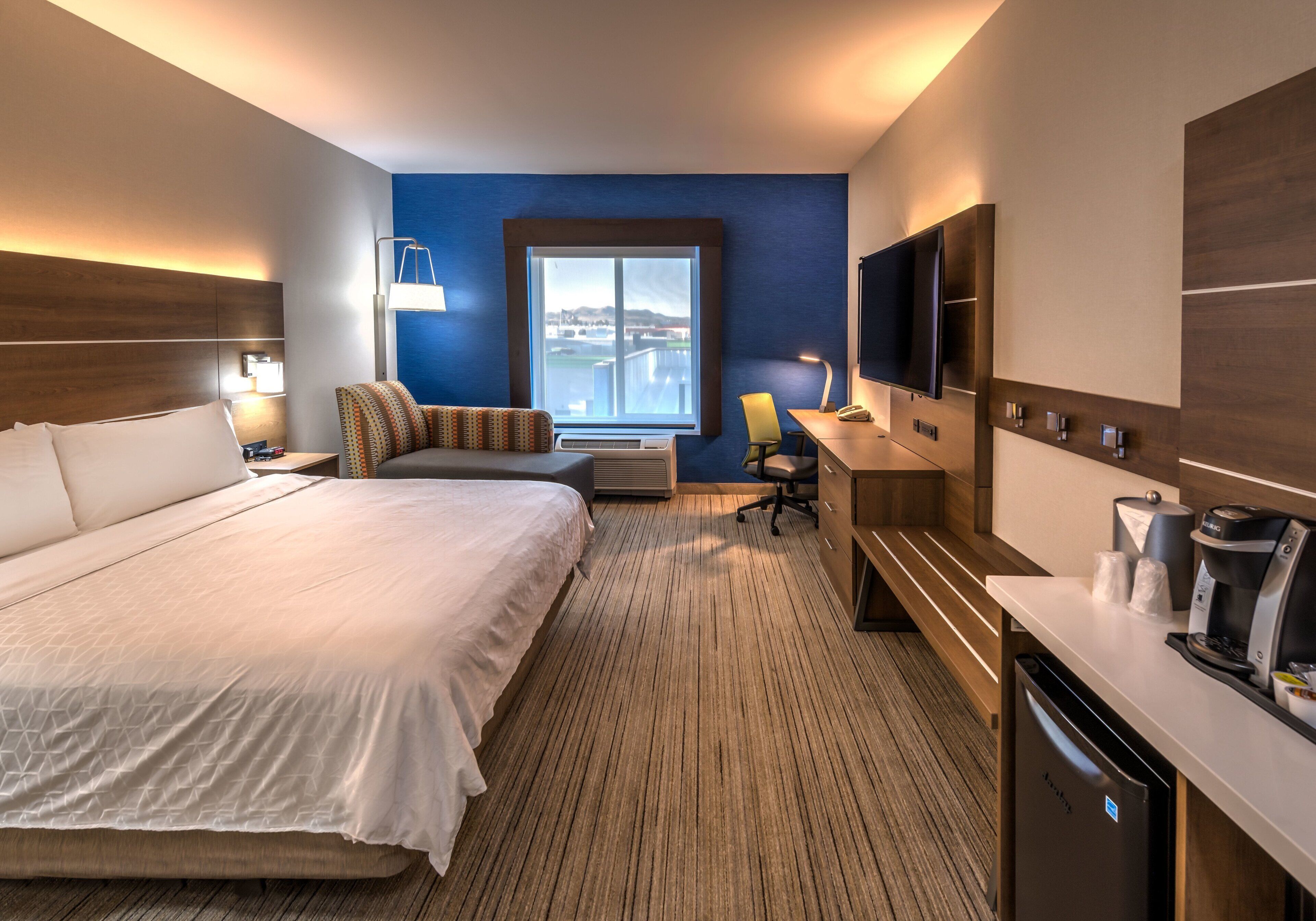 A hotel room with a large bed, a desk with a coffee maker, a TV, and a window with a view.
