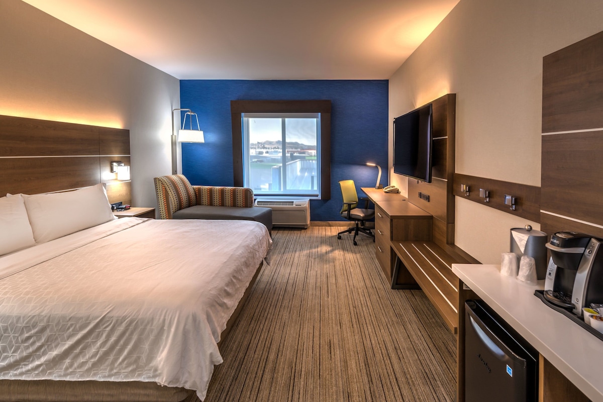 Ein Hotelzimmer mit einem großen Bett, einem Schreibtisch mit Kaffeemaschine, einem Fernseher und einem Fenster mit Aussicht.