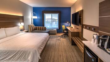 A hotel room with a large bed, a desk with a coffee maker, a TV, and a window with a view.