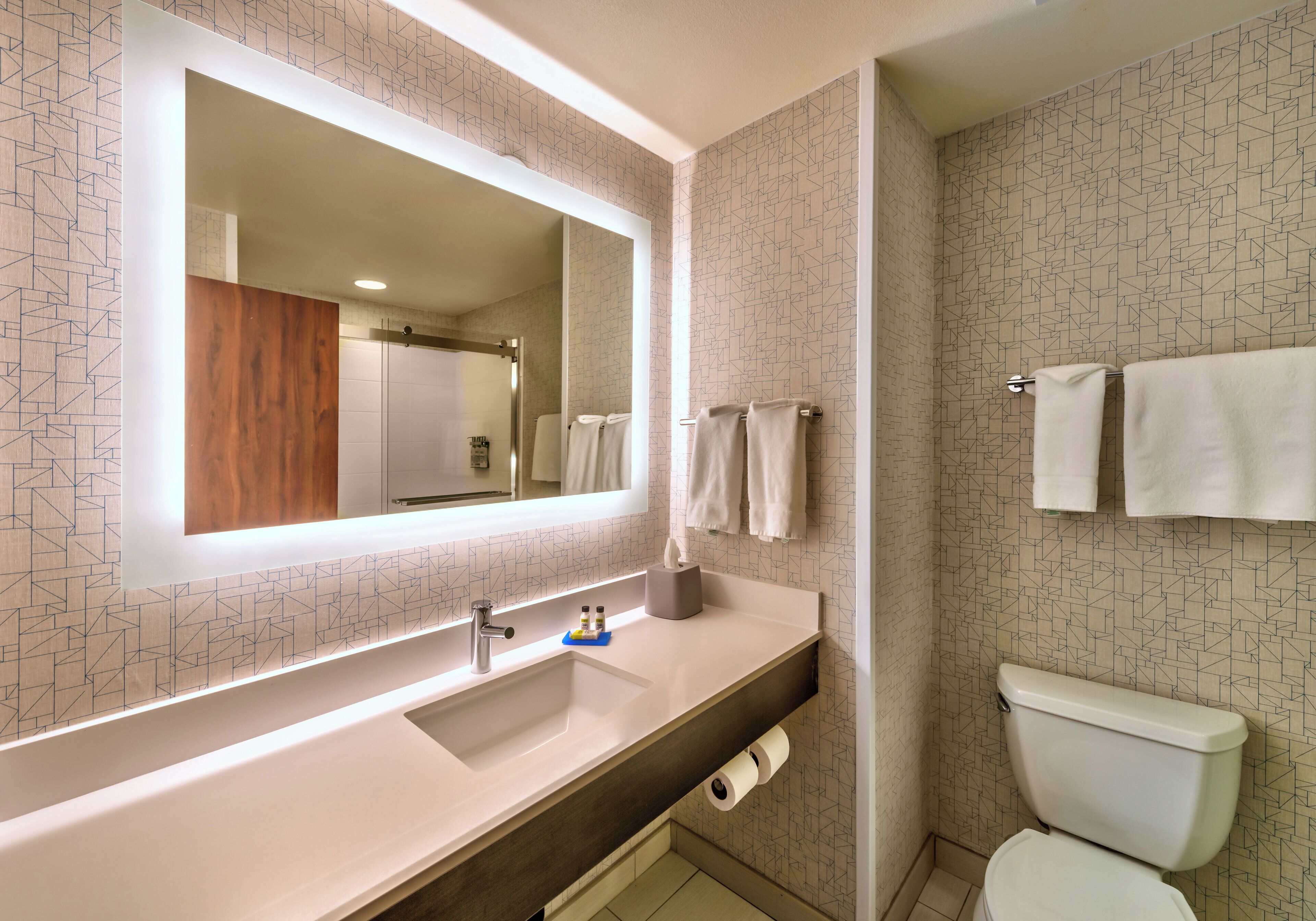 A modern bathroom with a large mirror, white sink, and toilet.