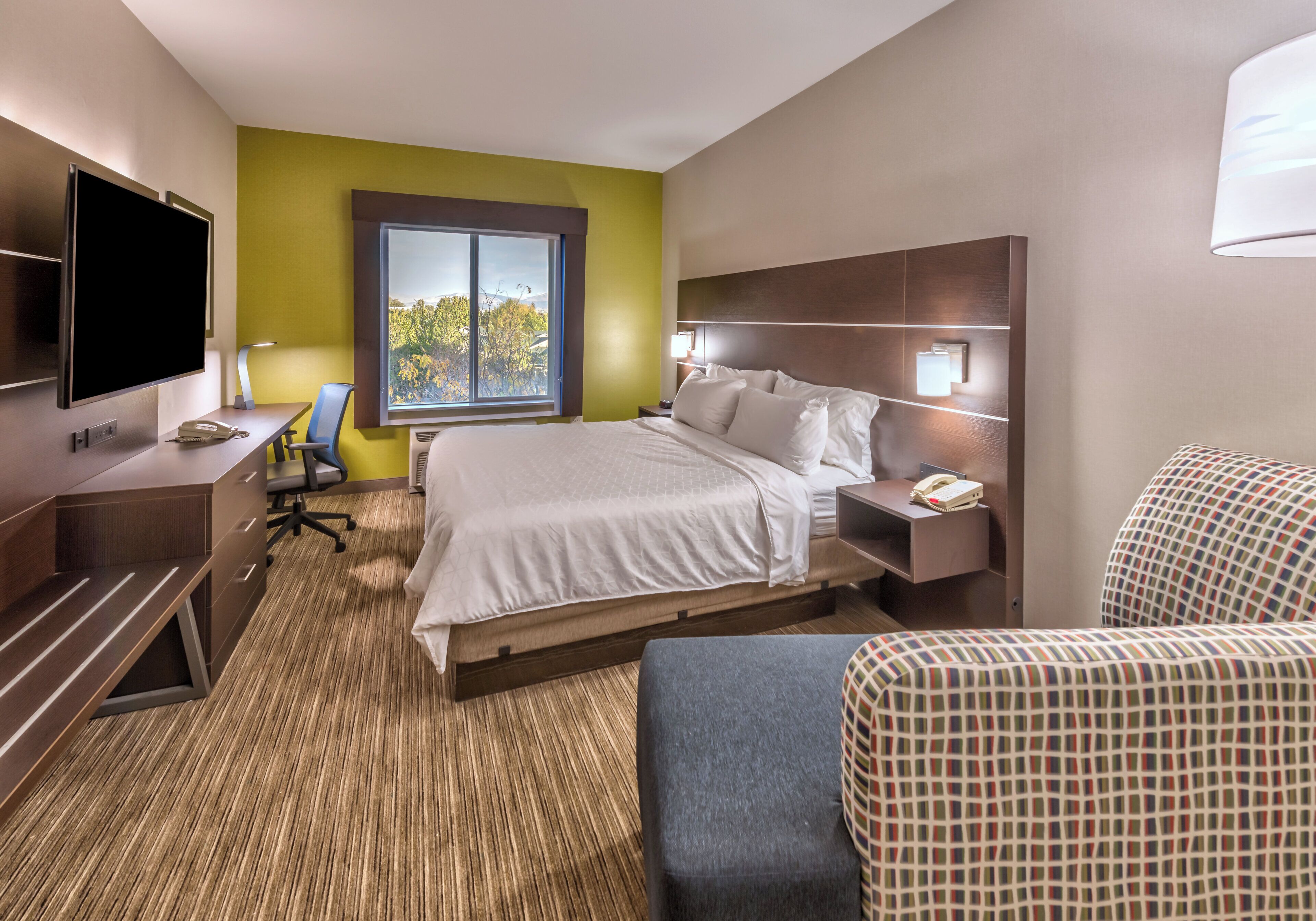 Een hotelkamer met een bed, bureau, stoel, televisie en een raam met uitzicht.
