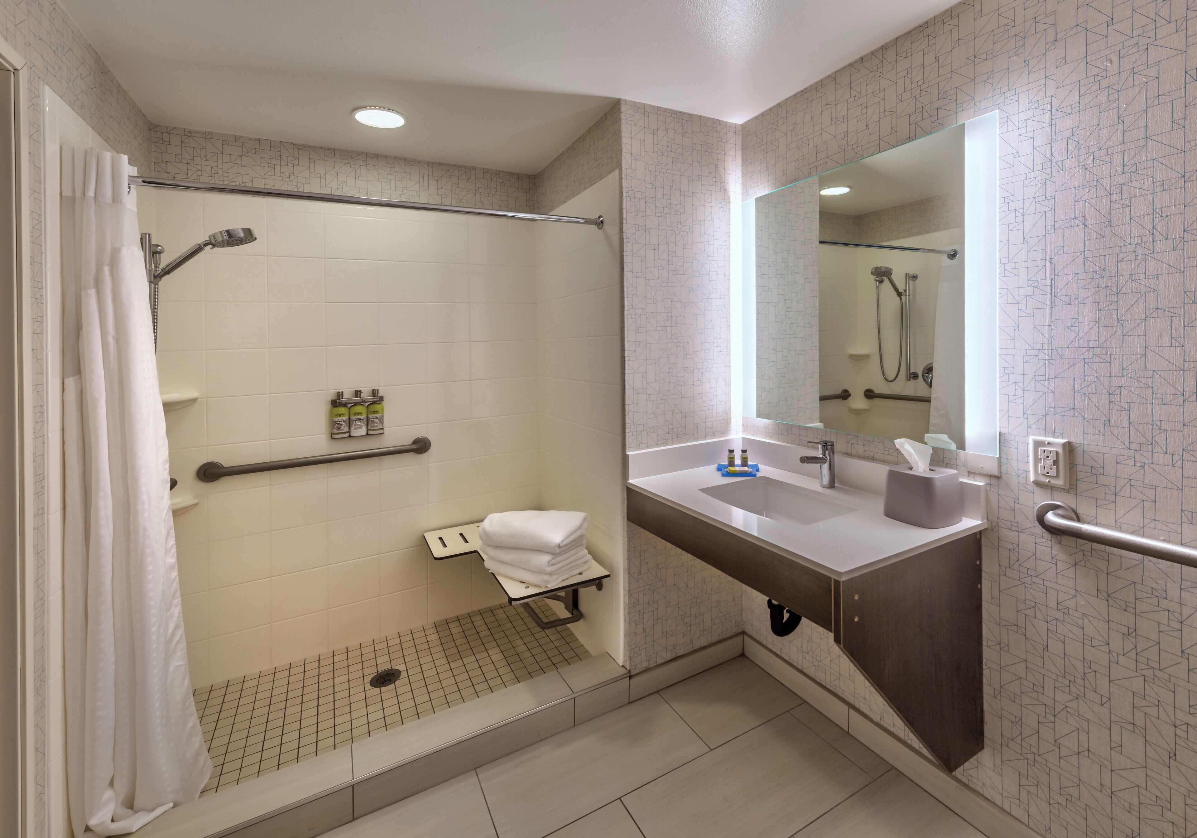 A modern bathroom with a walk-in shower, grab bars, a sink with a mirror, and a towel rack.