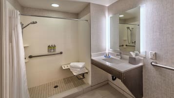 A modern bathroom with a walk-in shower, grab bars, a sink with a mirror, and a towel rack.